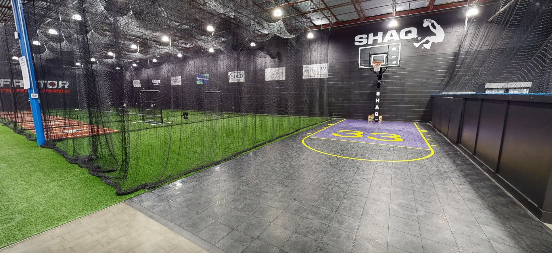 Interior of an indoor sports complex with a basketball court, artificial turf, and batting cages