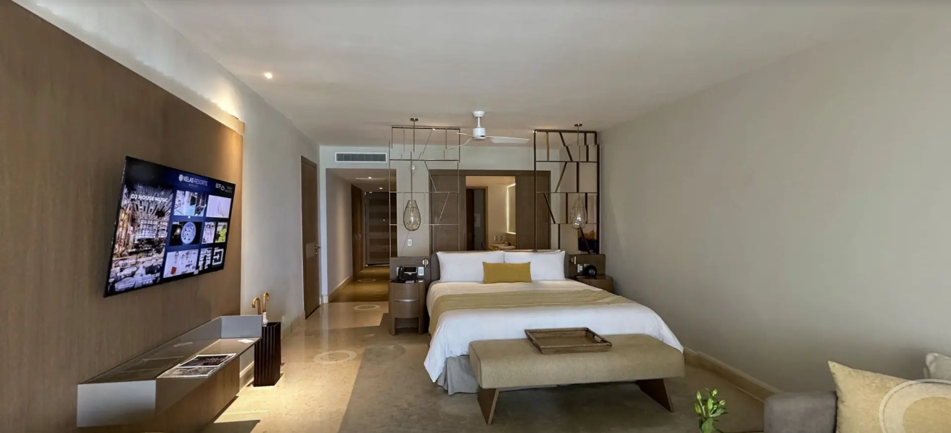 Interior of a resort suite with a king bed, ocean-view seating and a wall-mounted television